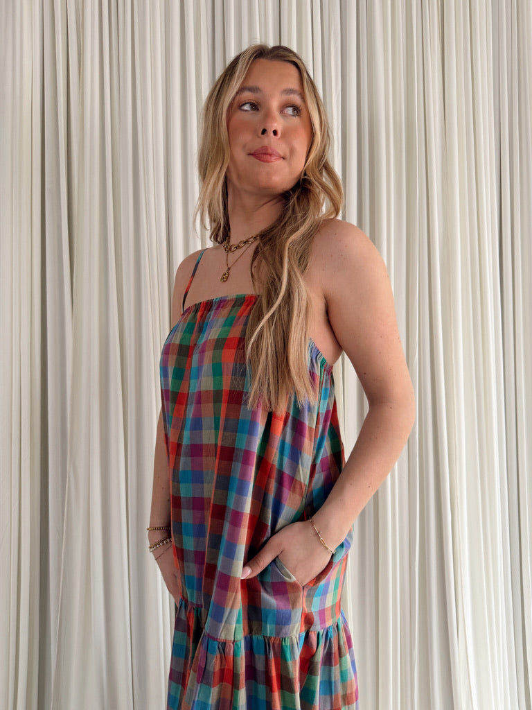 Woman wearing a colorful plaid dress against a neutral curtain background