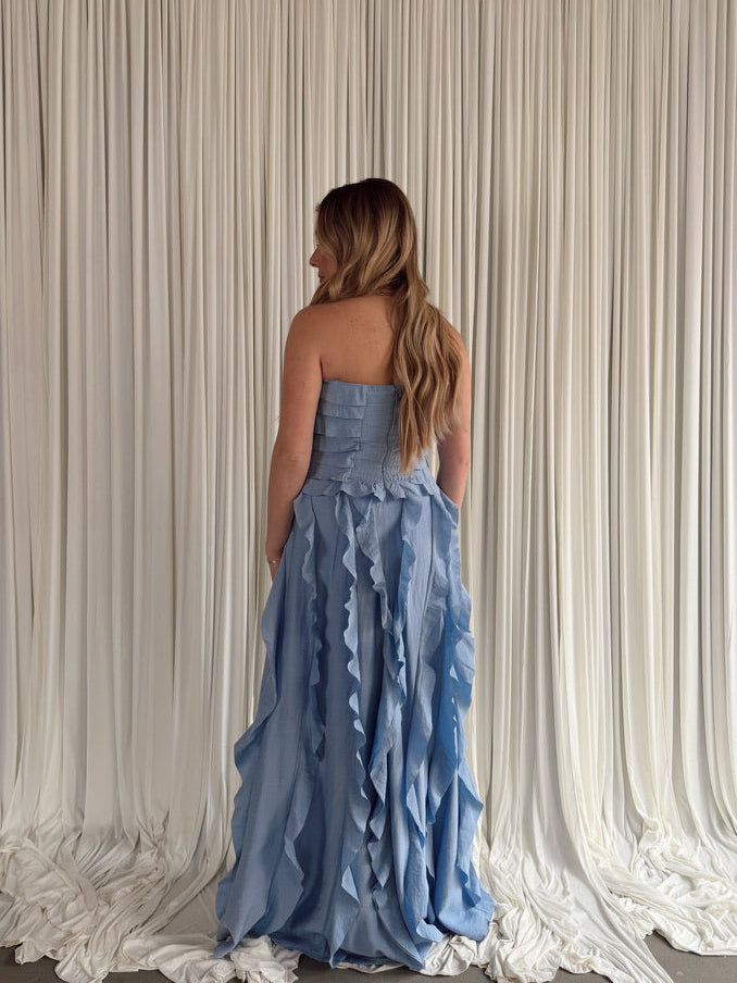Woman in a blue strapless gown standing in front of a white draped curtain.